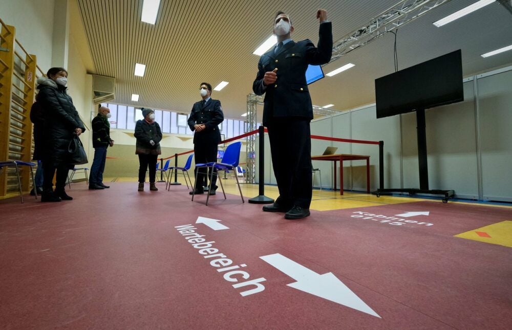 Daniel Schöppe erläutert den Ablauf im Impfzentrum. Über Markierungen auf dem Boden und einen großen Bildschirm werden die Impflinge geleitet.
