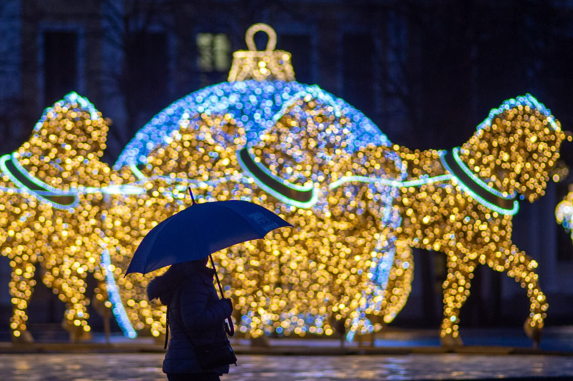 Ein Passant mit Regenschirm geht über den Magdeburger Domplatz an Figuren der Lichterwelt vorbei.