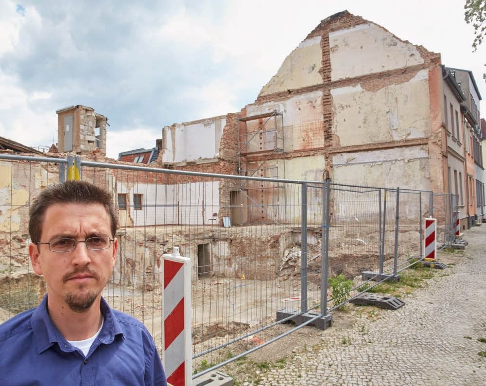 Marcus Holzhauer vor der Brachfläche, auf der einst das „Haus der Werktätigen“ stand. Die Giebelwand vor seinem Elternhaus dahinter ist zu einem Streitpunkt zwischen den Nachbarn geworden.