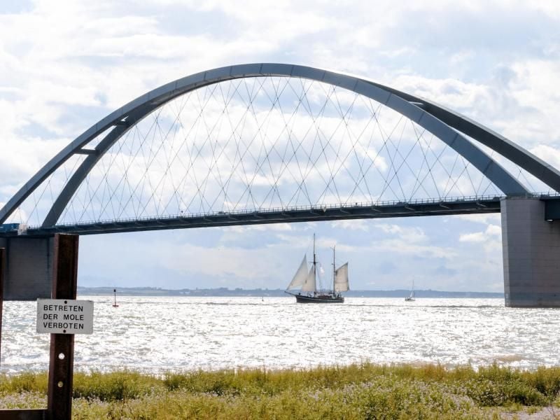 Ein Segelschiff fährt scheinbar unter der Fehmarnsundbrücke hindurch. Foto: M. Scholz/Archiv