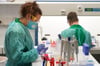 Eine Labor-Mitarbeiterin in Berlin hält hält ein Teströhrchen für einen Abstrichtest und eine Blutprobe in den Händen.