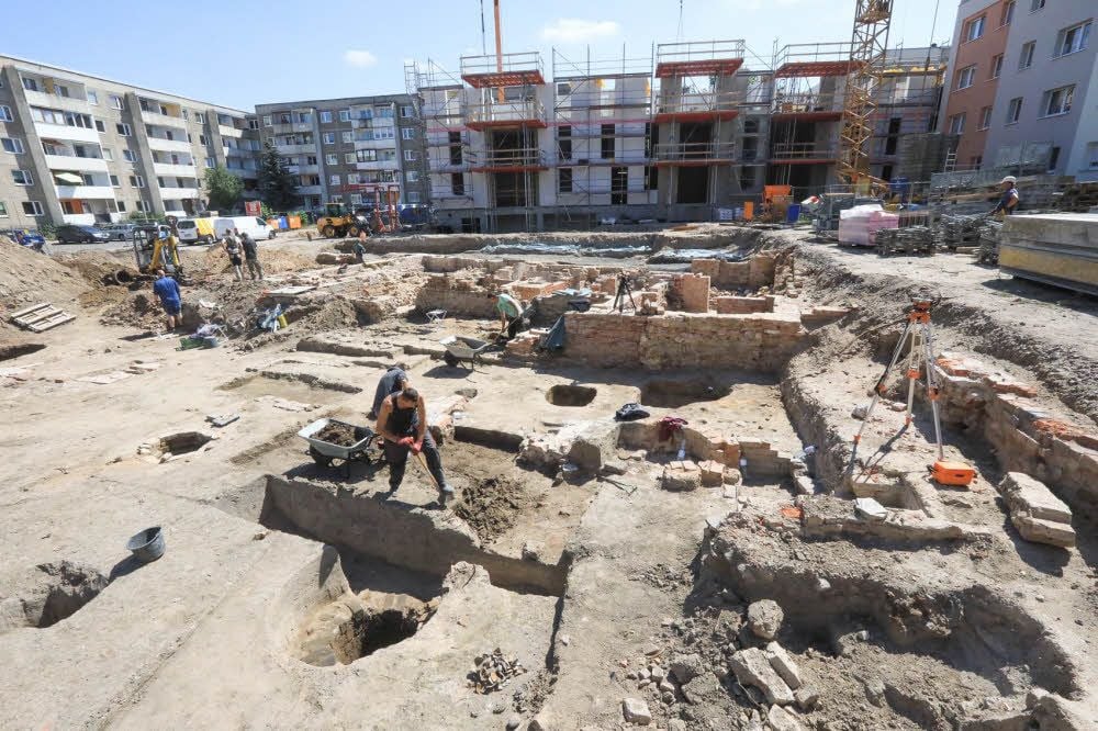 Die Archäologen und Grabungshelfer legen Häuser und Keller der Gründerzeit frei. Im Hintergrund nimmt der Neubau Gestalt an.