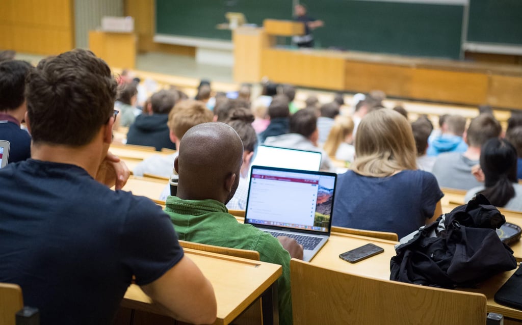 Studierende sitzen während einer Vorlesung mit Laptops im Hörsaal einer Uni.