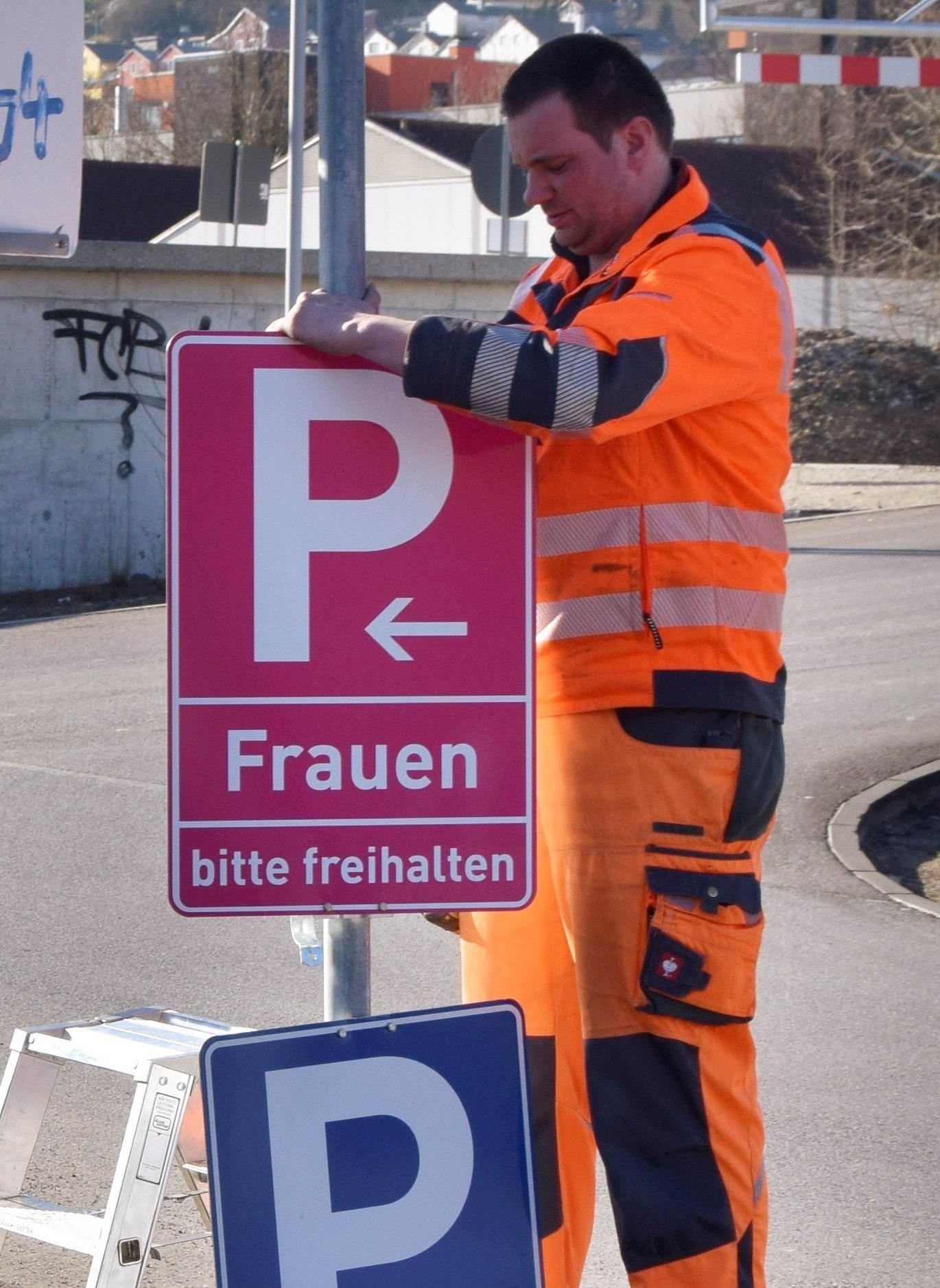 Ein Mitarbeiter der Stadt montiert an einem Parkplatz ein neues, pinkfarbenes Verkehrsschild.
