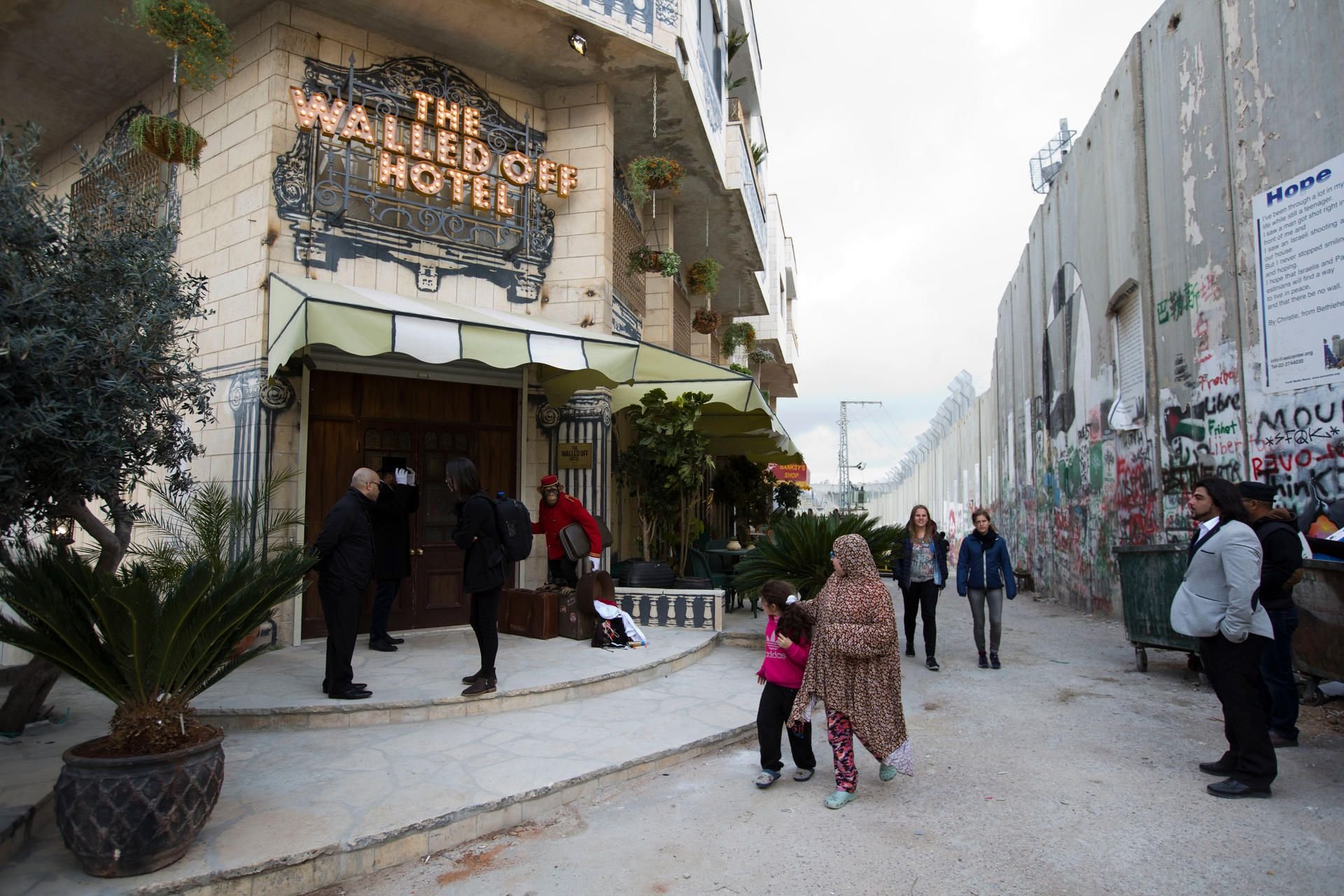 Passanten gehen am 03.03.2017 in Bethlehem (Westjordanland) am Eingangsbereich des «The Walled Off Hotel» und israelischen Sperranlagen vorüber. Das Hotel in der Nähe der israelischen Sperranlagen zeigt Motive des Künstlers Banksy und wirbt mit dem «schlechtesten Blick der Welt». Das Hotel öffnet am 11.03.2017.