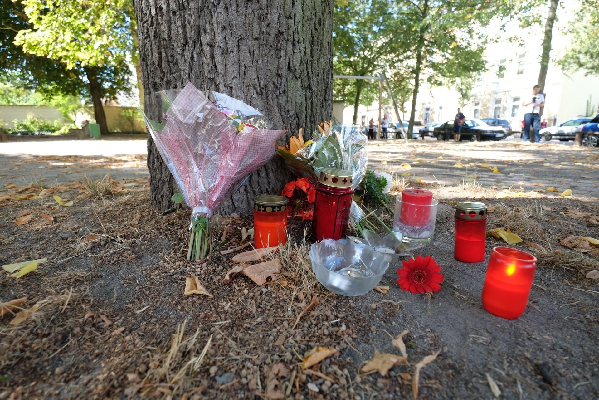 Köthen: Blumen und Kerzen stehen an einem Baum auf einem Spielplatz.
