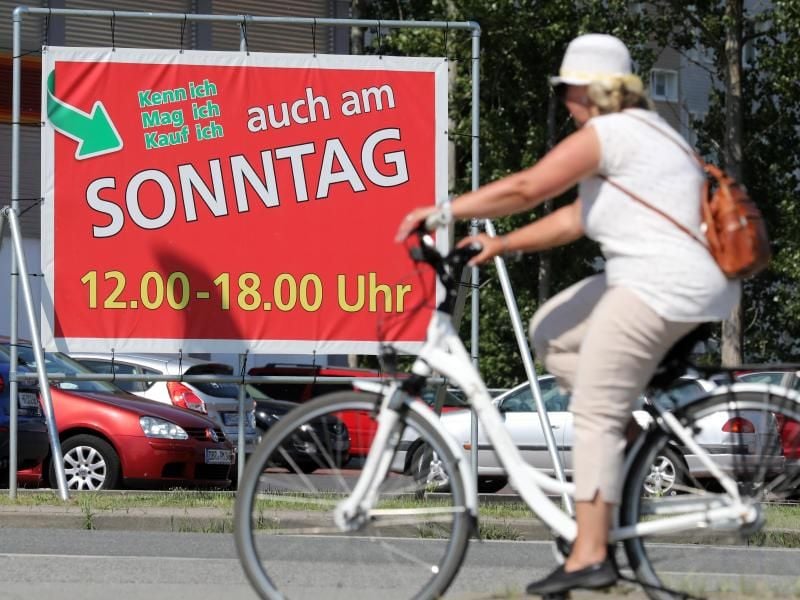 Eine Fahrradfahrerin fährt an einem Werbe-Transparent für Öffnungszeiten am Sonntag vorbei. Foto: Bernd Wüstneck/Archiv
