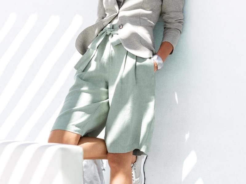 Bermudas sind eine Variante der kurzen Hosen, unterscheiden sich von klassischen Shorts aber durch ihre Länge. Sie eignen sich in Kombination mit einem Blazer auch fürs Büro - wie hier auch bei Madeleine zu sehen (ca. 120 Euro). Foto: Madeleine