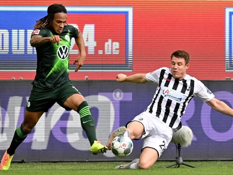 Wolfsburgs Kevin Mbabu (l) im Duell mit Dominique Heintz vom SC Freiburg. Foto: Sascha Steinbach/epa Pool/dpa