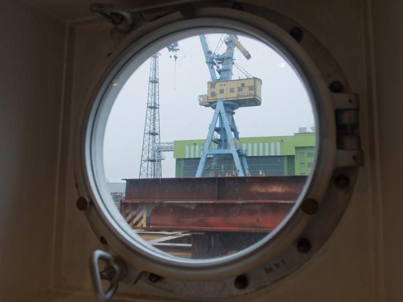 Blick aus einem Bullauge auf eine Werft. Foto: Stefan Sauer/Archiv
