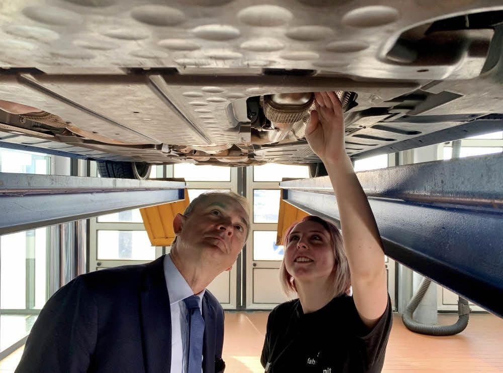 Annika Vesterling begutachtet mit Bildungsminister Marco Tullner den Unterboden eines Autos.