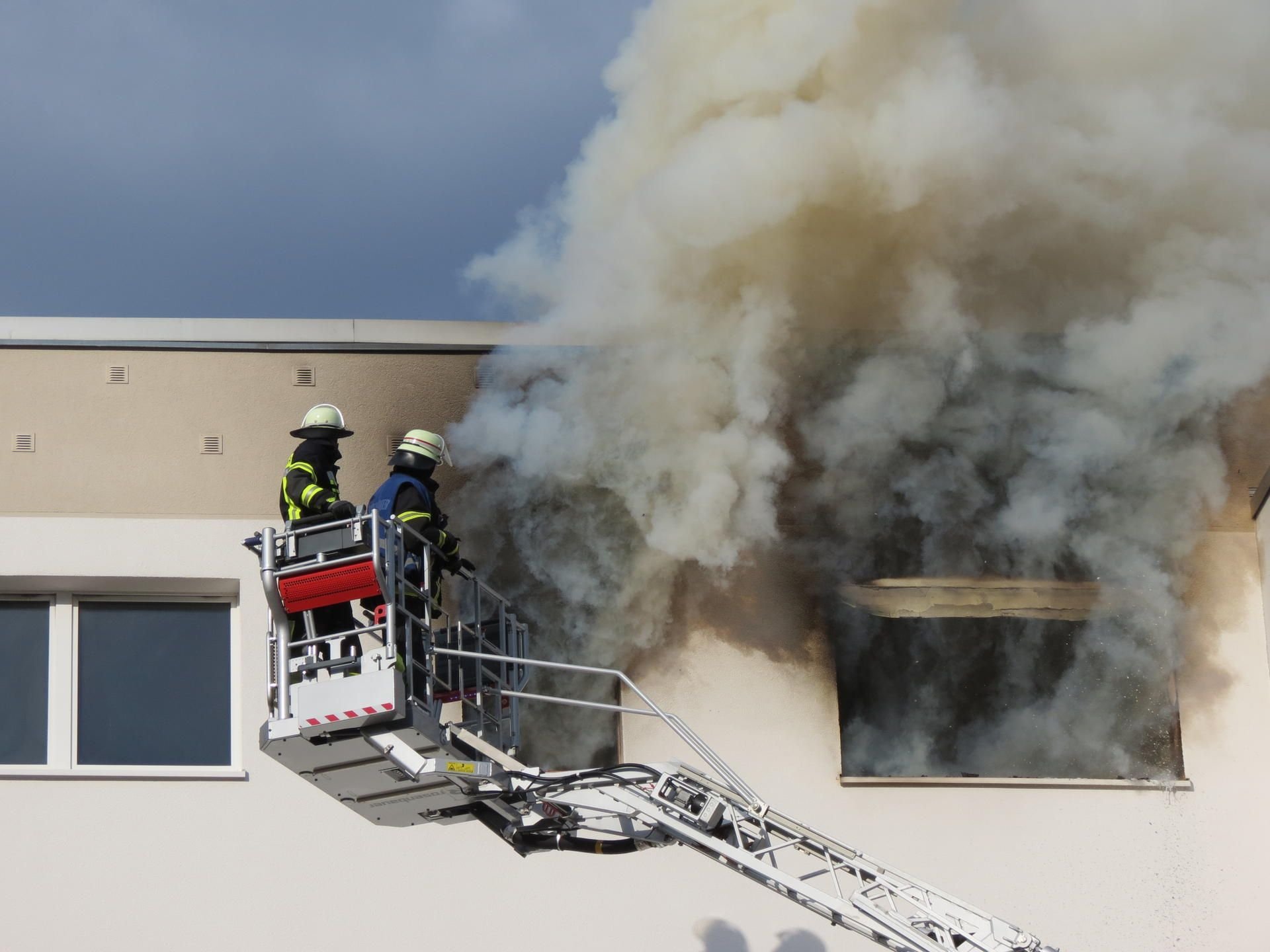 Feuerwehrleute löschen von einer Drehleiter aus den Wohnungsbrand in einem Mehrfamilienhaus.