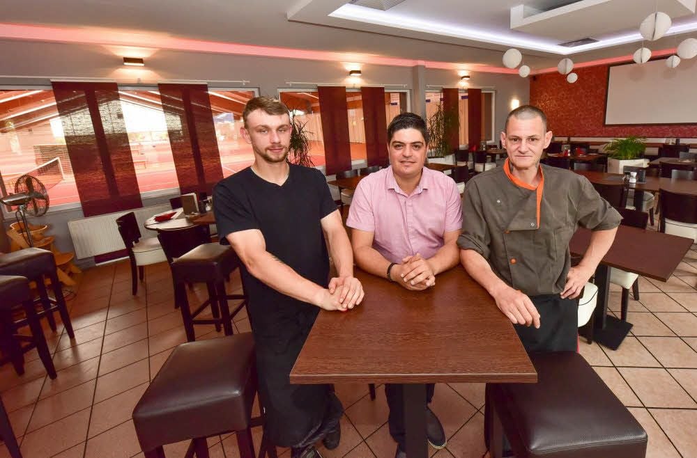 Ayhan Celik (M.) und seine Mitarbeiter Felix Alexander (l.) und Jörg Lindhardt sind zuversichtlich. Auch wenn die Gäste seines Lokals nun auf eine geschlossene Tennishalle schauen, geht es bei ihm weiter.