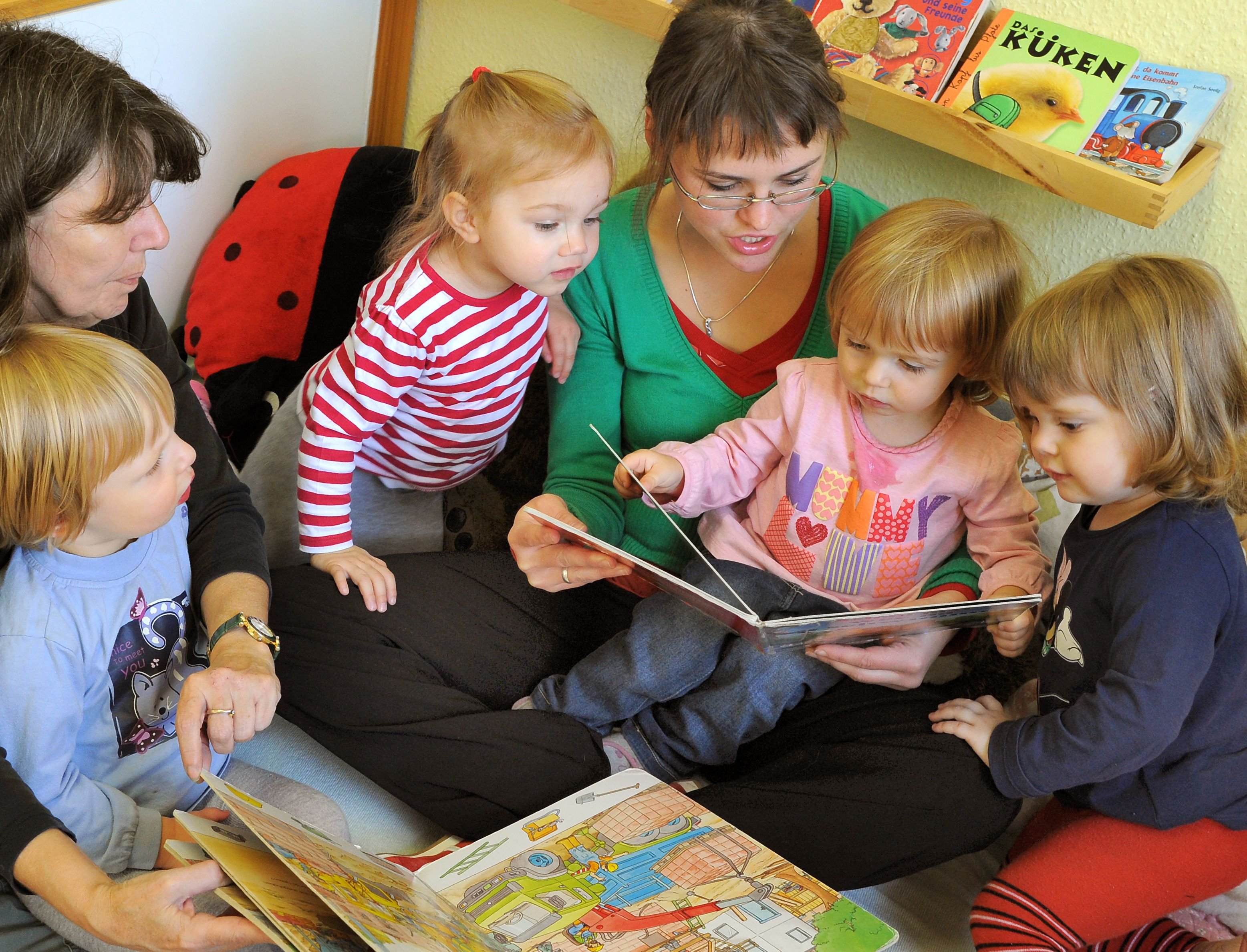 Kinder in einer Kindertagesstätte schauen sich zusammen mit einer Logopädin Bücher an.