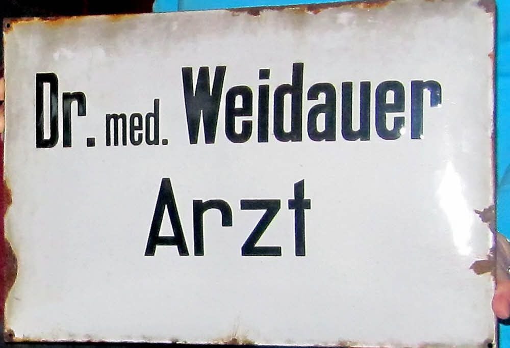 Angelika Wolter (geb. Dümichen, Enkelin der Weidauer-Helferin Meta Dümichen) hat dieses Schild der vormaligen Seydaer Arztpraxis von Joachim Weidauer bis heute aufgehoben. Ihr Vater Günther hatte es einst abgeschraubt. Angelika Wolter möchte das Schild, so die Kinder von Joachim Weidauer nichts dagegen haben, dem Seydaer Heimatverein für dessen Museum überlassen.