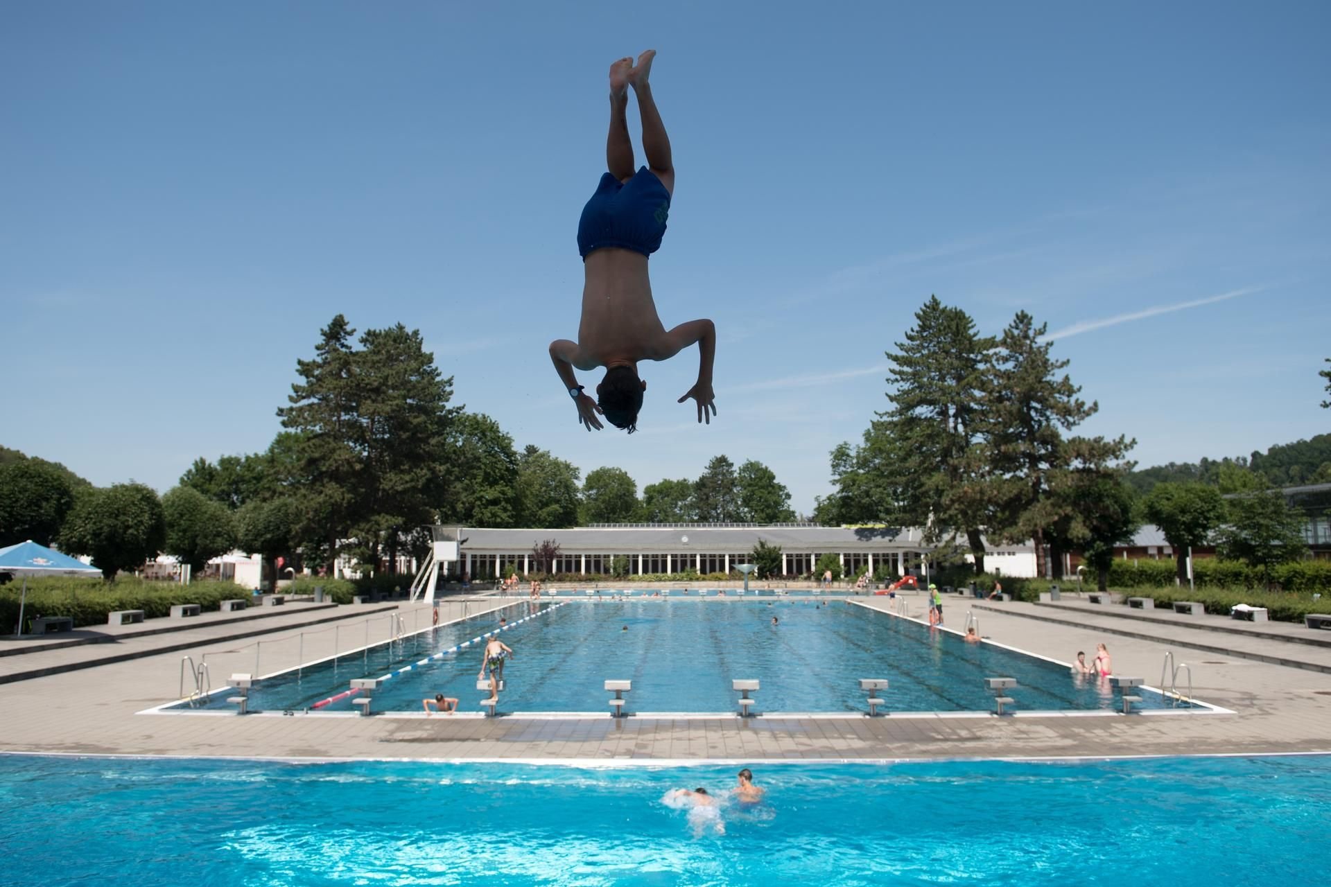 Ein Badegast springt in einem Schwimmbad vom 5-Meter-Turm ins Wasser.