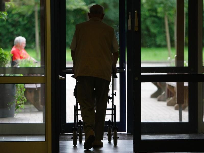 Ein Senior geht mit einer Gehilfe durch eine Tür in einem Altenheim. Foto: Peter Steffen/dpa/Symbolbild