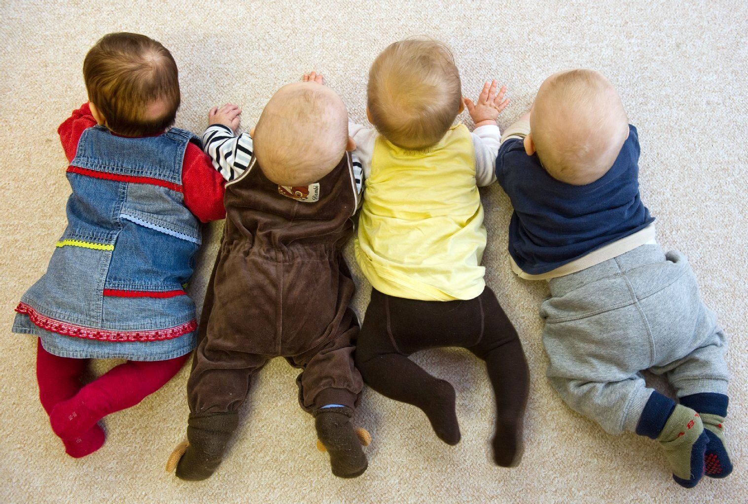Vier Babys liegen in einer Kita nebeneinander.