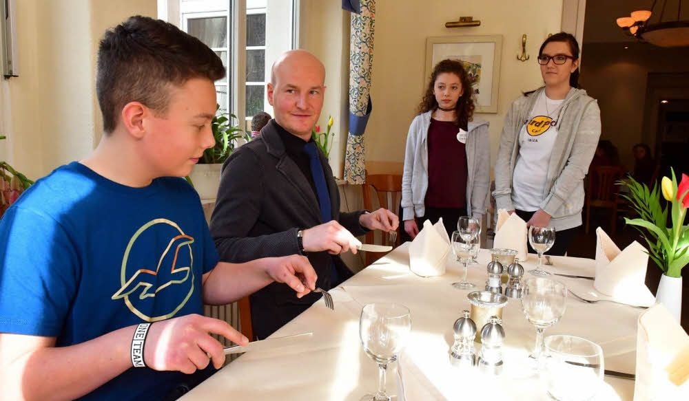 Lutz Mokros (Mitte) erklärt Max Kühling und anderen Jugendlichen im Hotel Güldene Berge, wie das Besteck richtig gehalten wird.