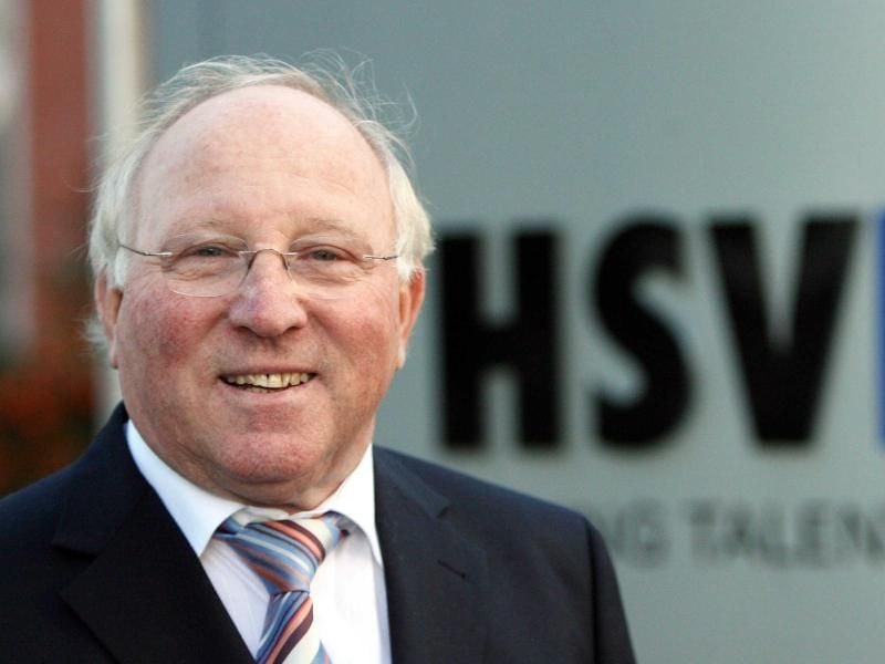 Uwe Seeler lächelt vor dem Logo des Hamburger SV. Foto: Maurizio Gambarini/Archiv