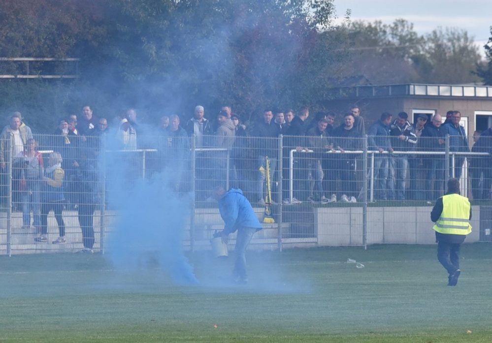 Ordner des SV Blau-Weiß Zorbau sammeln Rauchfackeln ein, die zuvor aus dem Weißenfelser Gästeblock aufs Spielfeld geschmissen worden.