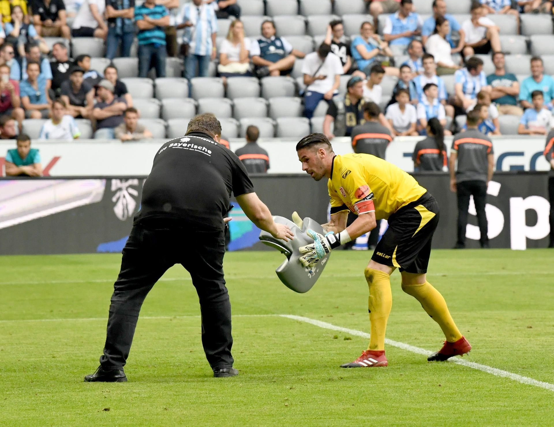 Ein Ordner und Torwart Philipp Pentke von Regensburg heben eine Sitzschale auf, die im Relegations-Rückspiel in München auf das Spielfeld geworfen wurde.