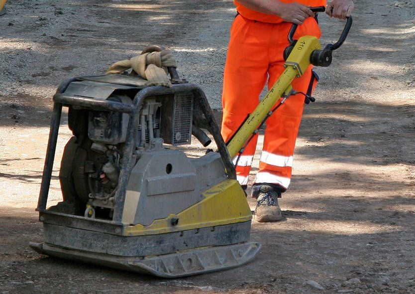 Straßenbau - Ein Straßenbauarbeiter verdichtet den Belag mit einer Rüttelplatte.