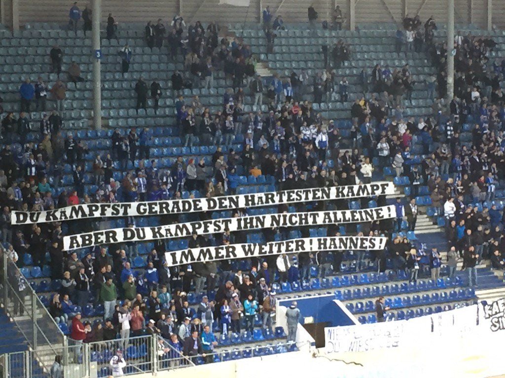 Fans des 1. FC Magdeburg halten Transparente hoch, auf denen sie Genesungswünschen an den verunglückten Hannes S. senden.