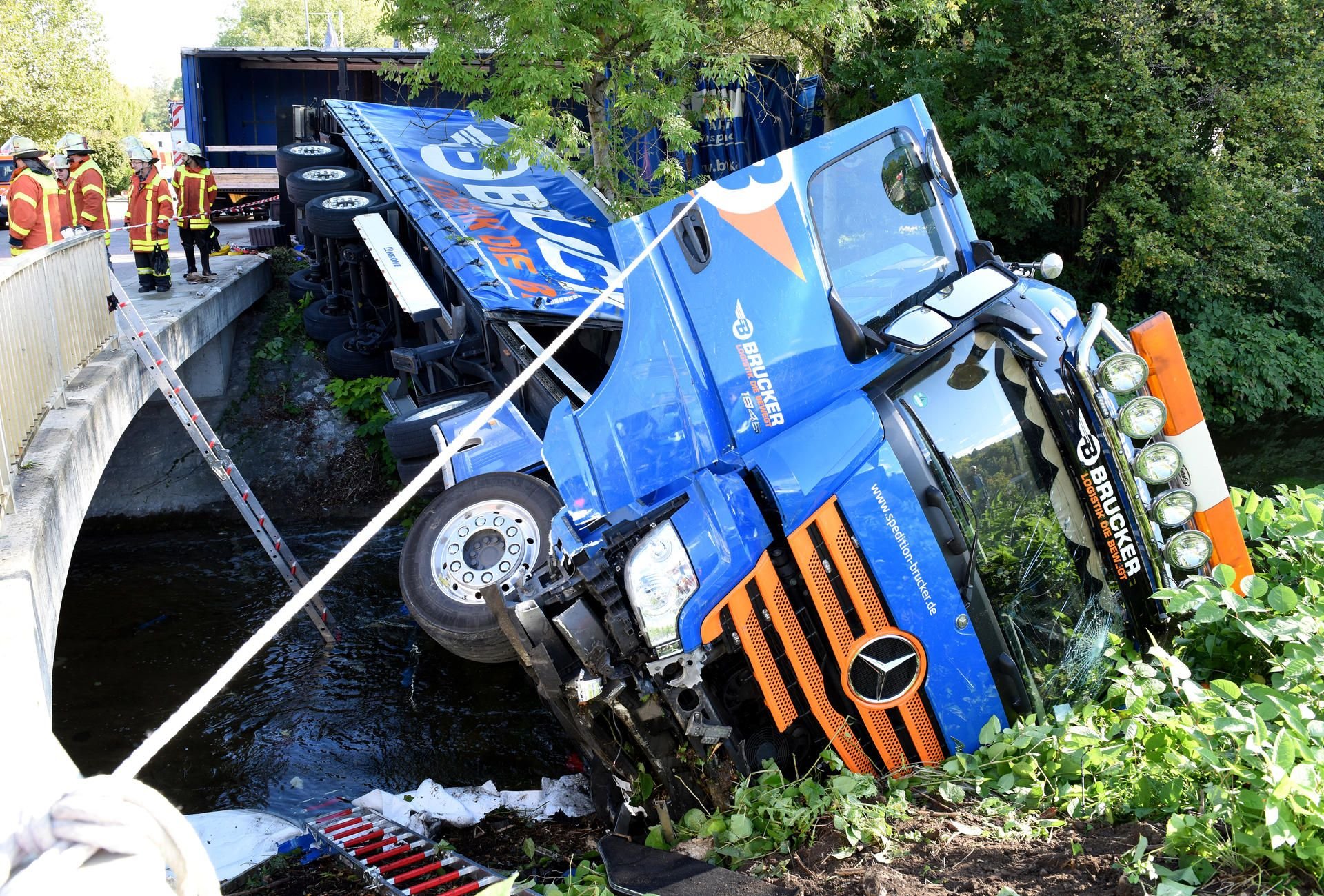 Aalen: Feuerwehrleute stehen neben einem Lastwagen, der in einen Fluss gekippt ist.