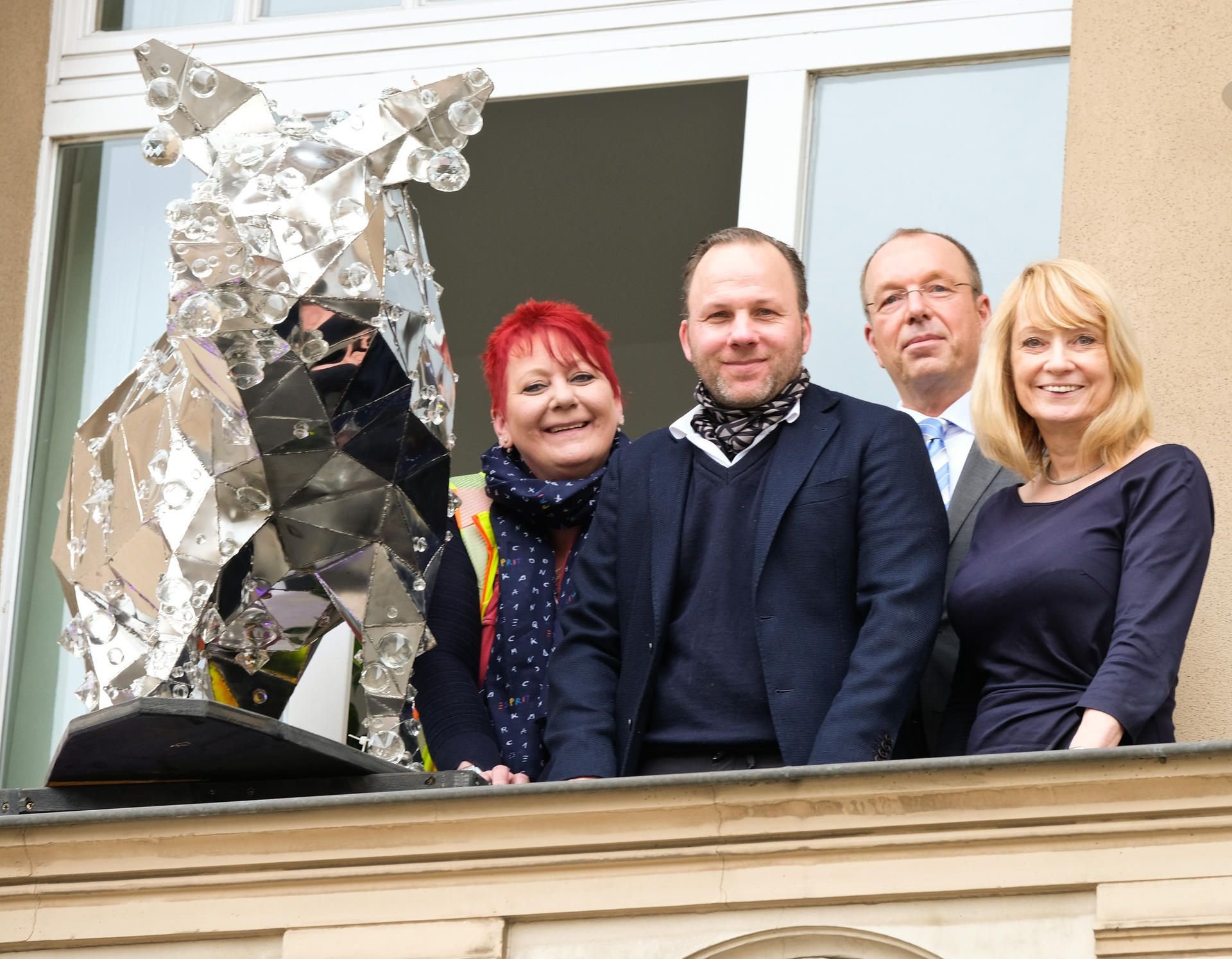 Von links nach rechts: Heike Knopf, Baustellenleiterin Havag, Künstler Marc Fromm, Uwe Foppe, Rechtsanwalt, und Petra Sachse, Leiterin DLZWWD, präsentieren am 11. April auf einem Balkon in der Wilhelm-Kuelz-Strasse in Halle eine kleine Version seines Glitzerschweins.