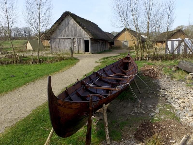 Ein Boot steht vor Häusern des Wikinger-Museums Haithabu. Foto: Carsten Rehder/Archiv