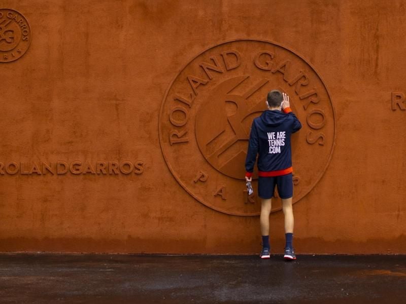 Ein Balljunge berührt das Logo vom Stade Roland Garros. Foto: Peter Dejong/AP/dpa
