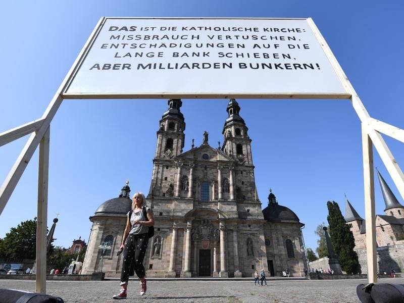 Ein Plakat der Giordano-Bruno-Stiftung mit der Aufschrift "DAS ist die Katholische Kirche: Missbrauch vertuschen. Entschädigungen auf die lange Bank schieben. Aber Milliarden bunkern !" steht am Rande der Herbstvollversammlung der Deutschen Bischofskonferenz auf dem Platz vor dem Dom. Foto: Arne Dedert/dpa