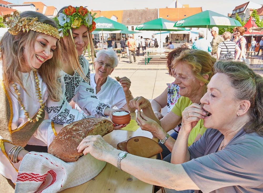Gelebte Völkerverständigung: Die gebürtige Russin Anna Dalinger (links) und ihre ukrainische Kommilitonin Alona Riabokin verteilen unter den Gästen des Europäischen Stationenweges auf dem Bernburger Karlsplatz in der Region hergestelltes Brot und Salz.