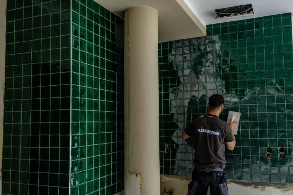 Die sind neu. Ein Fliesenleger verfugt die dunkelgrüne Wand.