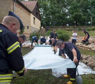 Einsatzkräfte der Feuerwehr aus Aken verteilen in Langenstein ein Vliestuch auf einem Hang.
