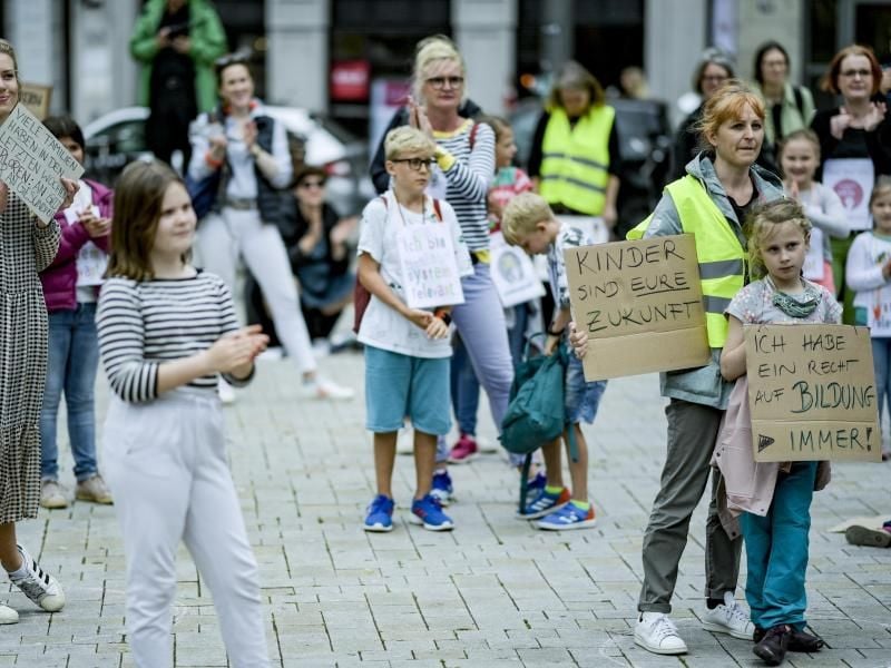 Eltern und Kinder stehen mit Schildern mit der Aufschrift „Kinder sind eure Zukunft“ und „Ich habe ein Recht auf Bildung - immer!“ auf dem Gänsemarkt. Foto: Axel Heimken/dpa