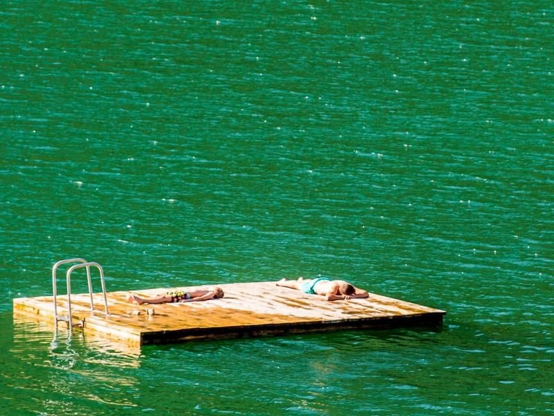 Zwei Männer liegen auf einem Schwimmponton im Wasser des Sylvensteinstausee bei Lenggries. Foto: Lino Mirgeler