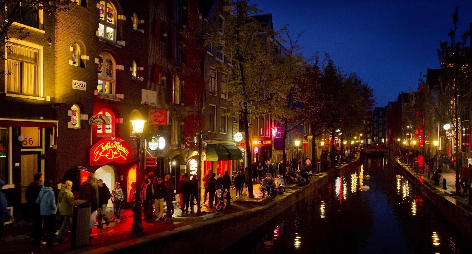 Menschen schlendern am Abend an einer Gracht entlang durch den Rotlichtbezirk De Wallen.