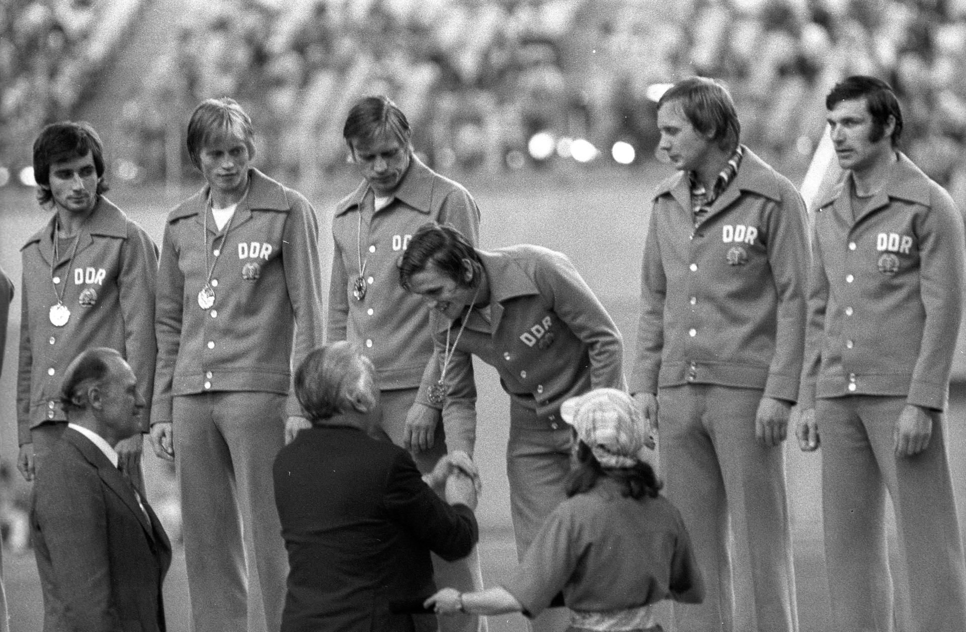 Die Olympiasieger Reinhard Häfner, Hans Jürgen Riediger, Bernd Bransch, Martin Hoffmann, Gerd Kische und Wolfram Löwe (v.l.n.r.) werden am 31. Juli 1976 in Montreal von FIFA-Präsident Joao Havelange (vorn li.) und IOC-Präsident Lord Michael Killanin geehrt.