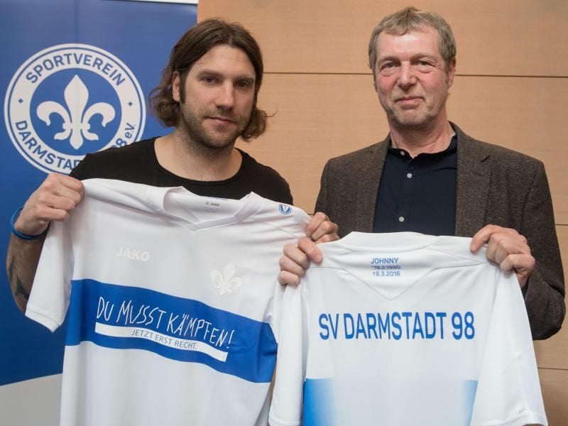Trainer Torsten Frings (l) präsentiert ein Sondertrikot zum ersten Todestag von Jonathan Heimes zusammen mit dessen Vater Martin. Foto: Frank Rumpenhorst