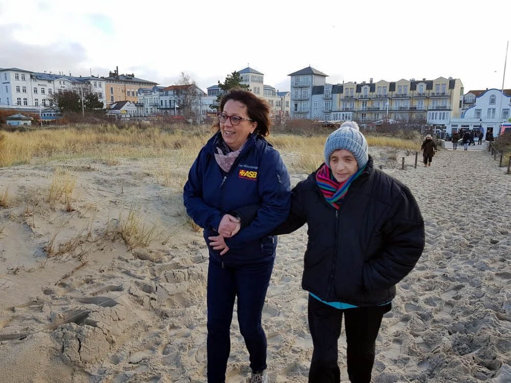 Irena Glass und eine Ehrenamtliche des ASB gehen am Strand spazieren.