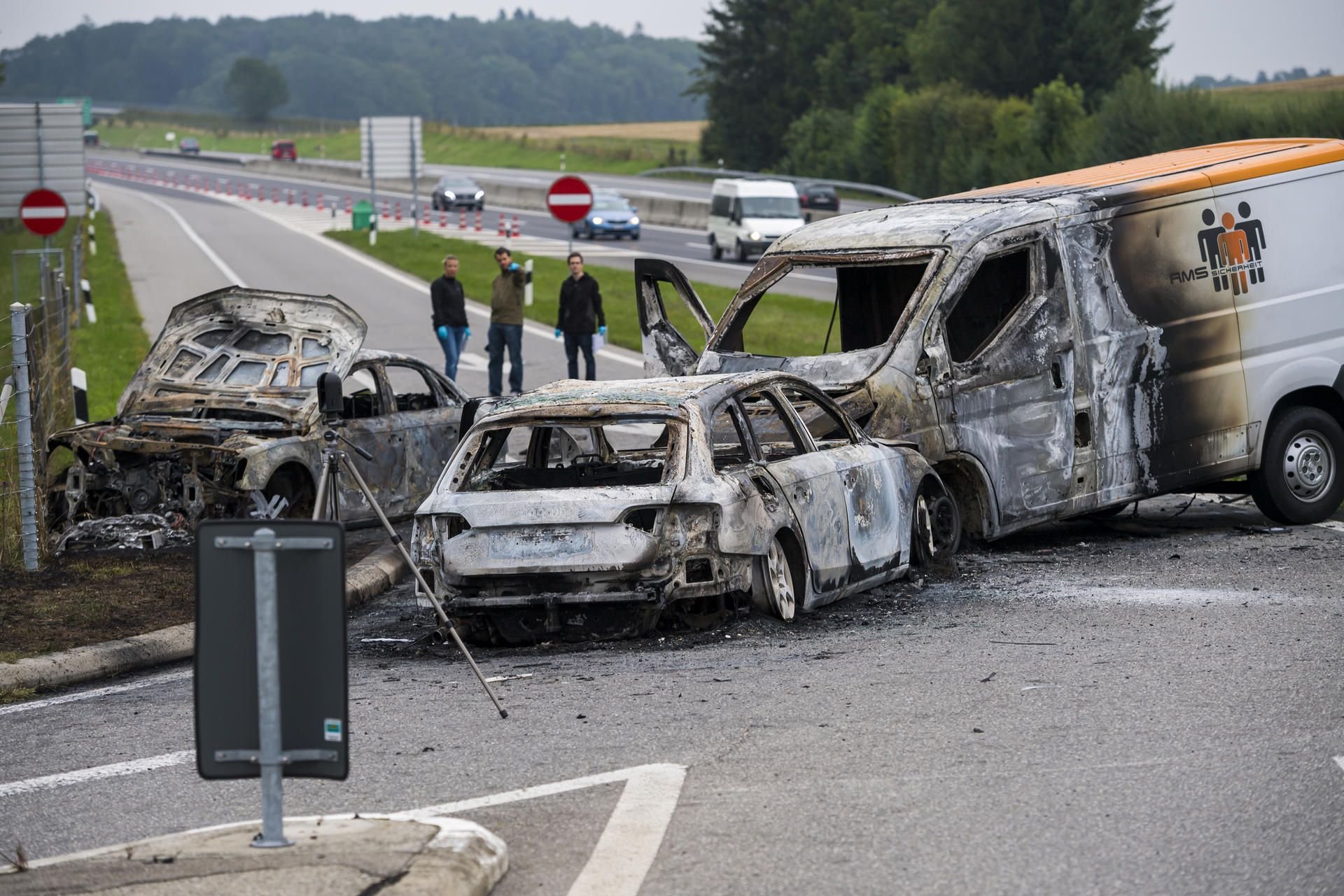 Kriminalbeamte untersuchen nach einem Überfall drei ausgebrannte Fahrzeuge an der Ausfahrt La Sarraz (Schweiz).