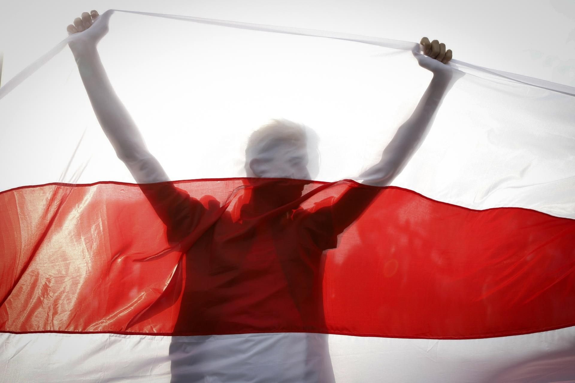 Belarus, Minsk: Ein Demonstrant hält eine historische belarussische Fahne. Trotz eines Großaufgebots an Sicherheitskräften haben Zehntausende Menschen gegen den autoritären Staatschef Lukaschenko demonstriert