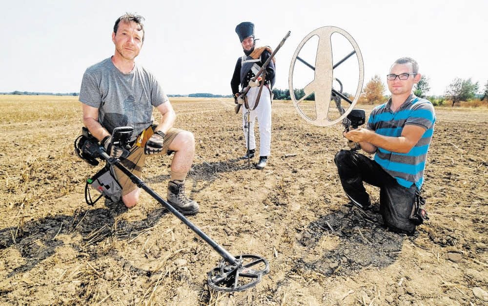Die Archäologen Michael Cahill (links) und Michael Schmahl (rechts) hocken mit Metalldetektoren auf einem Acker in Leipzig-Holzhausen.
