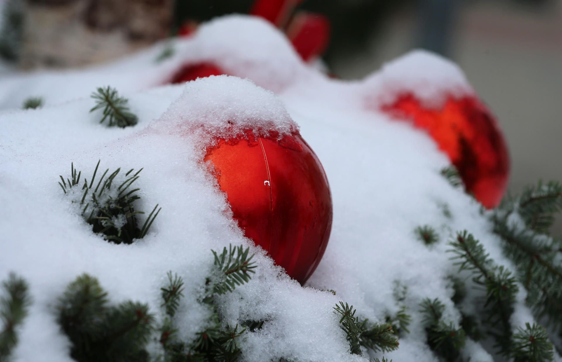 Christbaumkugeln an einem weihnachtlich geschmückten Brunnen sind mit Schnee bedeckt