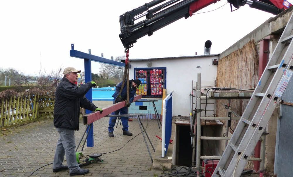 Vereinschef Jörg Schneider (oben, links) und Mario Kutzler befestigen am Kran den Eisenträger, der für das neue Kiosk-Vordach montiert wird.