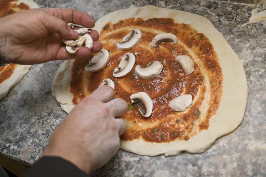 Massimo Caraccioli belegt eine Pizza hier mit Pilzen, Zwiebeln und etwas Gemüse. Dann kommt sie für wenige Minuten in den Ofen. Fertig!