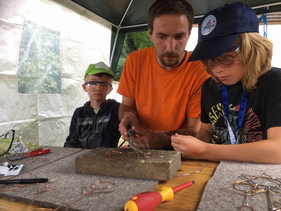 Dominik Heerwagen zeigt Tristan (7, li.) und Lenny (10, re.) in der Metall-Werkstatt, wie man ein Strichmännchen aus Metall lötet.