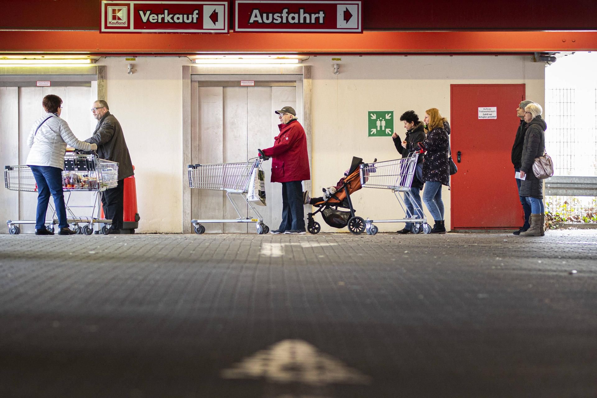 Menschen stehen mit ihren Einkaufswägen vor einem Supermarkt an.